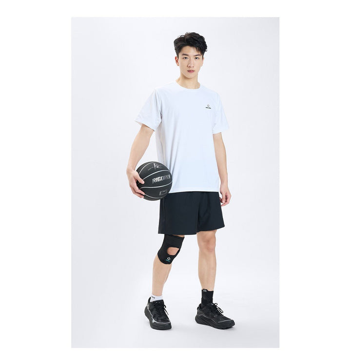 Model in a white tee and black shorts holding a basketball, wearing the Rigorer adult sports knee support brace on his left knee